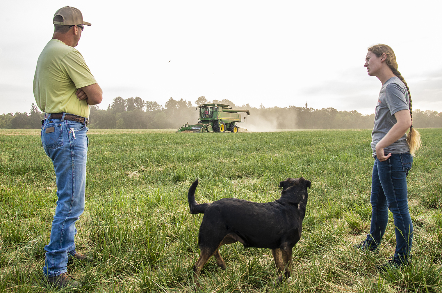 Extension faculty talking in agricultural field with farmer with dog nearby