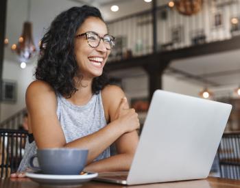 woman of color laughing and at table with laptop and coffee